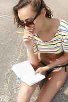 female makes notes and sitting on the beach photo