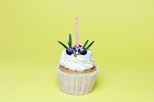 birthday cupcake with one burning candles over yellow background photo