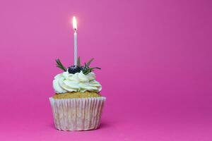 birthday cupcake with one burning candles over pink background photo