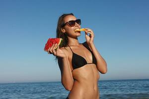 Summer vacation - young girl eating fresh watermelon on sandy beach photo