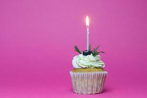 birthday cupcake with one burning candles over pink background photo