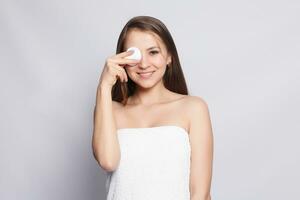 Happy smiling beautiful young woman cleaning skin by cotton pad. photo