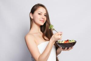 hermosa morena niña en toalla comiendo Fresco ensalada y sonriente foto