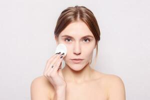 Happy smiling beautiful young woman cleaning skin by cotton pad. photo