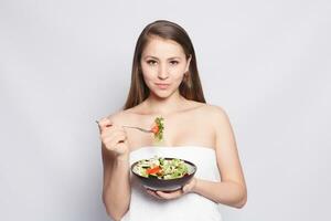 Beautiful brunette girl in towel eating fresh salad and smiling photo