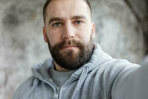 barbado hombre en un gris antecedentes hace un selfi foto