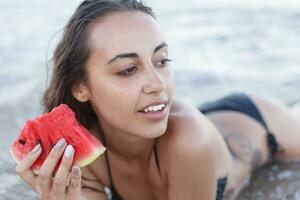 verano vacaciones - joven niña comiendo Fresco sandía en arenoso playa foto