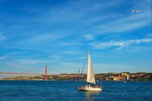 View of 25 de Abril Bridge over Tagus river, Christ the King monument and a yacht boat at sunset. Lisbon, Portugal photo