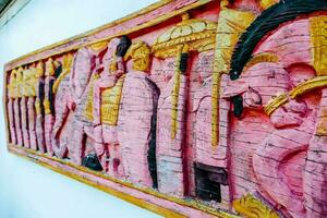 a pink wall with a wooden carving of people photo