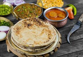 indio cocina chapati con sev tamatar, gatta curry, raita, papad o cebolla en de madera antecedentes foto