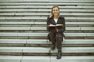 Beautiful businesswoman sitting on the staircase in the city and working. photo