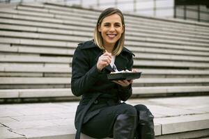 hermosa mujer de negocios disfruta descansando en un almuerzo descanso mientras sentado en el escalera en el ciudad. foto