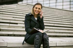 Businesswoman using phone and personal organizer while working outdoor. photo