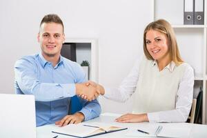 Businesswoman and businessman sitting in office and shaking hands. photo