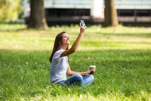 Beautiful businesswoman is resting at the park,taking selfie and drinking coffee. photo