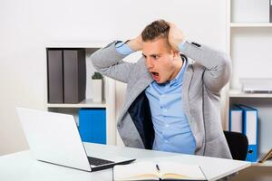 Businessman with laptop sitting at his office and he is in panic. photo