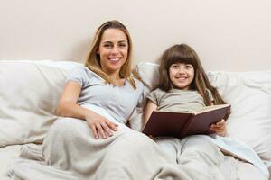 Mother and daughter reading together book in bed photo