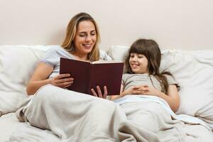 Mother and daughter reading together book in bed photo