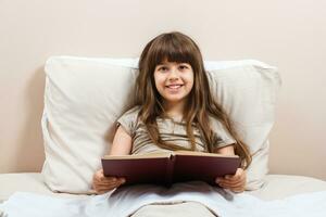 pequeño niña leyendo libro en cama foto