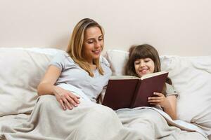 Mother and daughter reading together book in bed photo