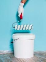 Image of paint can and man holding paint roller in front of blue wall. photo