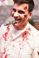 Man dressed up like a bloody zombie with a rat in his mouth at halloween celebration. photo