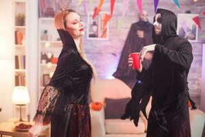 Man dressed up like a grim reaper dancing with beautiful vampire woman at halloween celebration. photo