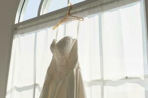 Elegant White bridal wedding dress hanging on wall photo