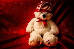 White soft plush toy baby little teddy bear in a red bow-tie sits on a background of burgundy curtain photo