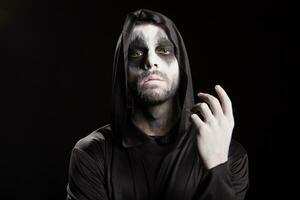 Spooky man dressed up like a grim reaper over black background. Halloween mystery. photo