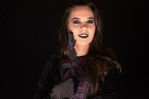 Attractive young woman dressed up like a gothic witch with a rose over black background for halloween. photo