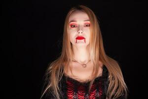 Beautiful blond woman dressed up like a vampire over black background. photo