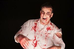 Cheerful man dressed up like a scary zombie over black background. Halloween creative makeup. photo