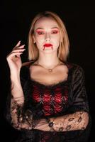 Blond woman dressed up like a vampire with blood on his lips over black background. Halloween costume. photo