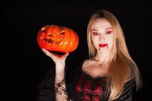 Portrait of beautiful girl dressed up like a vampire holding a pumpkin for halloween. photo