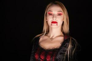 Beautiful vampire woman with dripping blood over black background. photo