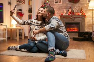 Happy couple smiling while taking a selfie on christmas day. Cat sleeping in the background. photo