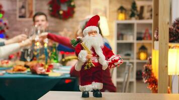 Santa claus in focus on the table with big family celebrating christmas in the background. Traditional festive christmas dinner in multigenerational family. Enjoying xmas meal feast in decorated room. Big family reunion photo