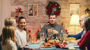 Head of the family opening a bottle of champagne at family reunion for christmas. Traditional festive christmas dinner in multigenerational family. Enjoying xmas meal feast in decorated room. Big family reunion photo