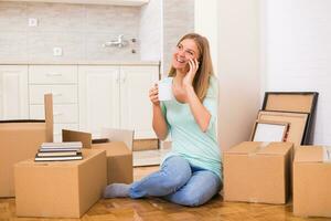 Beautiful woman drinking coffee and talking on the phone while moving into her new apartment. photo