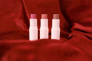 Lipstick on bright scarlet silk or maroon fabric background with soft folds, realistic cosmetic. Beauty Product. photo