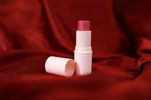 Lipstick on bright scarlet silk or maroon fabric background with soft folds, realistic cosmetic. Beauty Product. photo