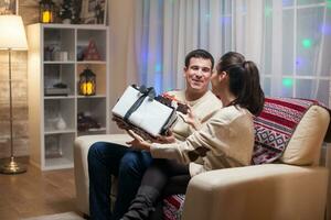 Young wife giving her husband a big present on christmas day. Happy couple. photo