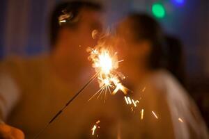 Young couple sitting on couch kissing and holding bengal lights on christmas day. photo