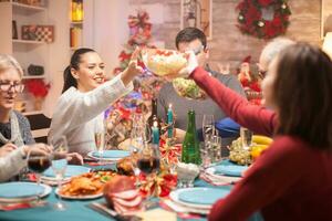 Happy woman passing the salad over the table to his daughter at christmas family dinner. photo