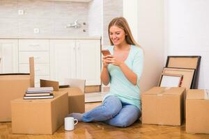 Beautiful woman using phone while moving into her new apartment. photo