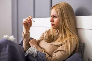 Exhausted woman having fever and checking temperature. photo