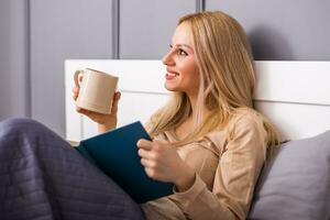 Beautiful woman enjoys reading a book at her bedroom and drinking tea or coffee. photo