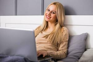 Beautiful woman enjoys using laptop at her bedroom . photo