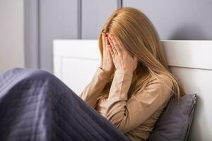 Sad woman covering her face while sitting on a bed. photo